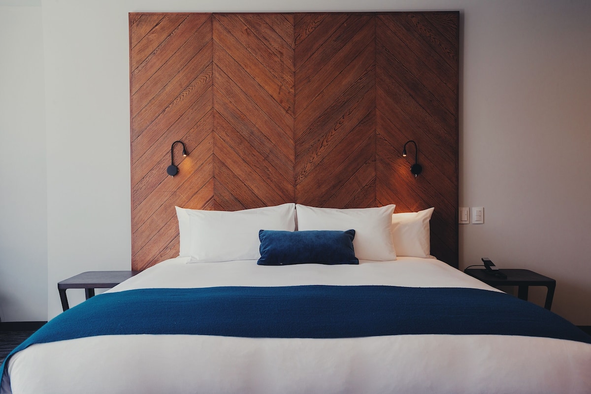 A neatly made bed with a wooden headboard, two bedside tables, and a blue throw blanket.