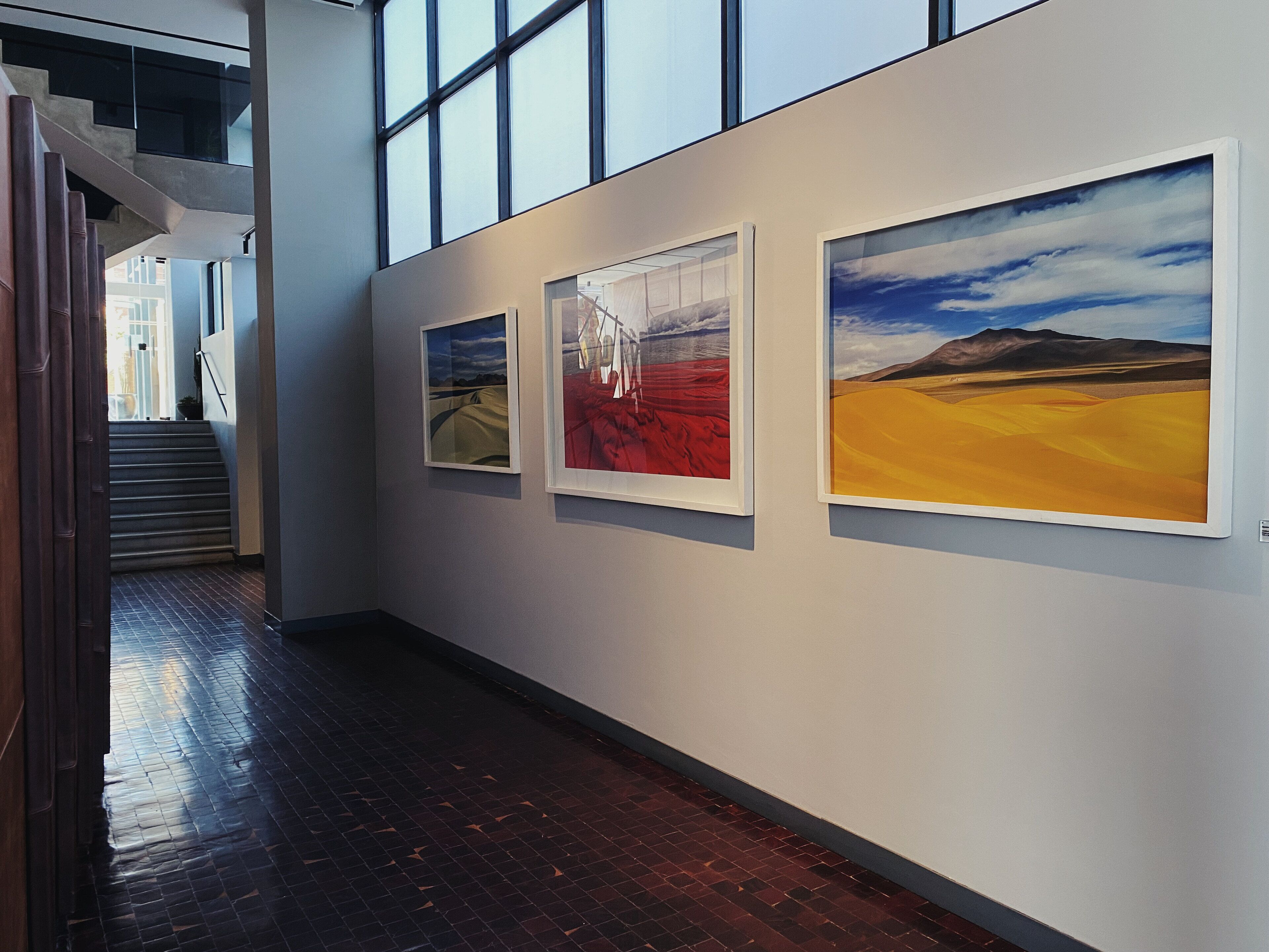 A hallway with three framed artworks on the wall, a staircase to the left, and a brick floor.