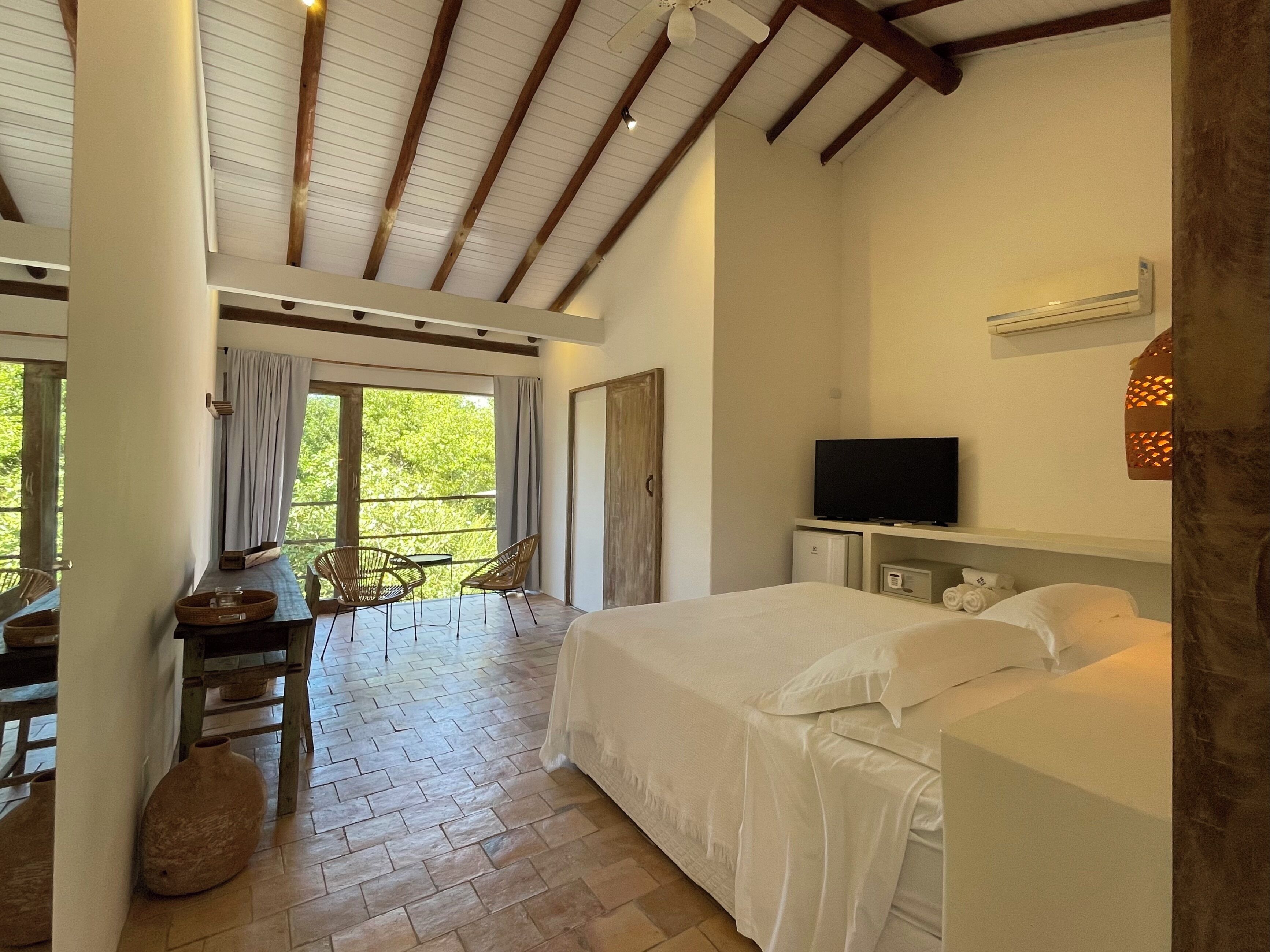 A bedroom with a large bed, a TV, and a balcony with chairs and a table.