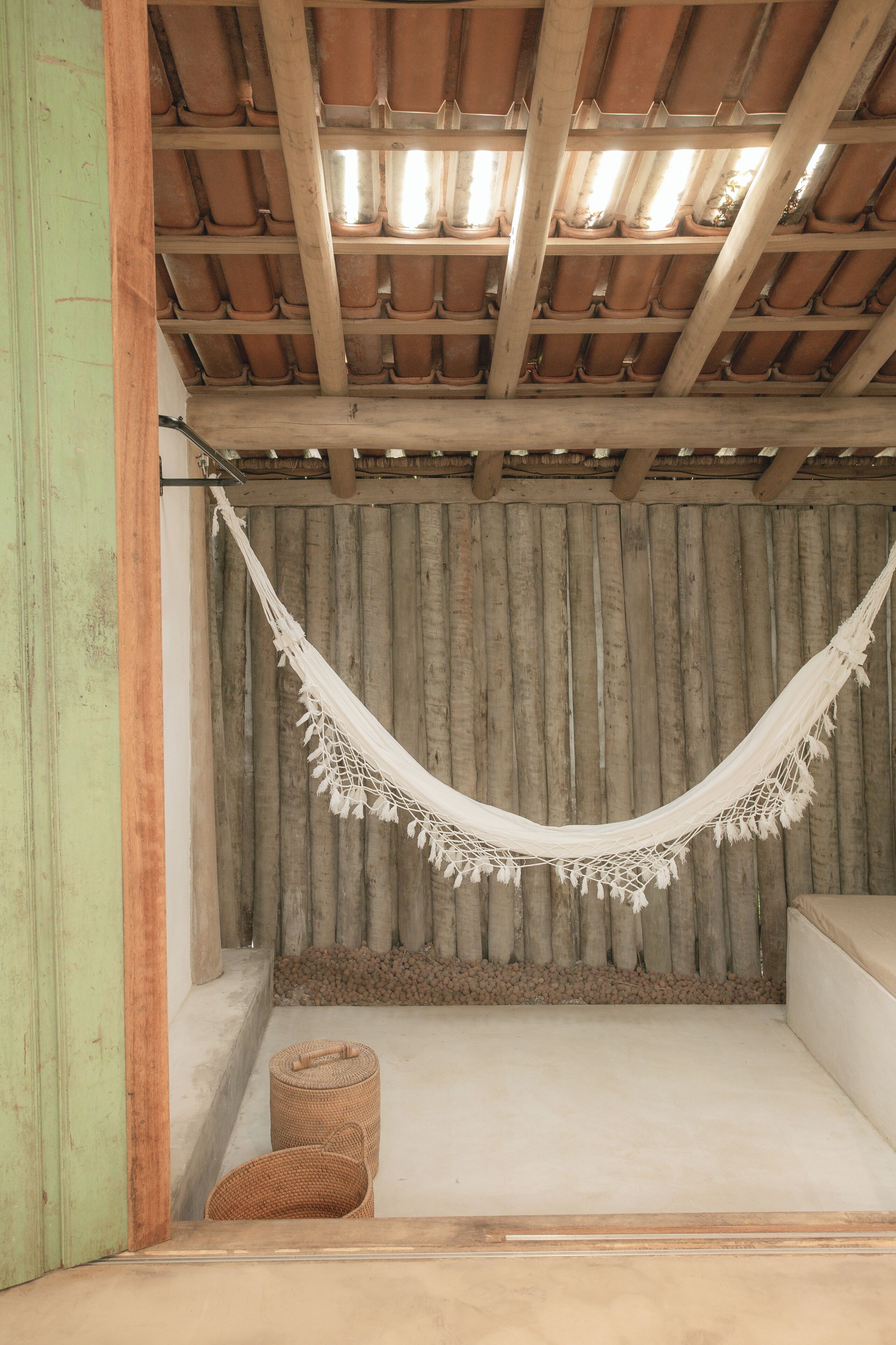 A hammock suspended from a wooden ceiling, a woven basket on the floor, and a corrugated metal wall.