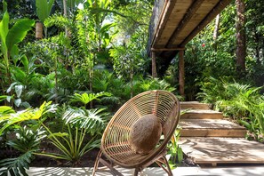 A wicker chair in a lush garden with a wooden staircase leading up to a covered area. - Pousada Seis e Meia (Porto Seguro)