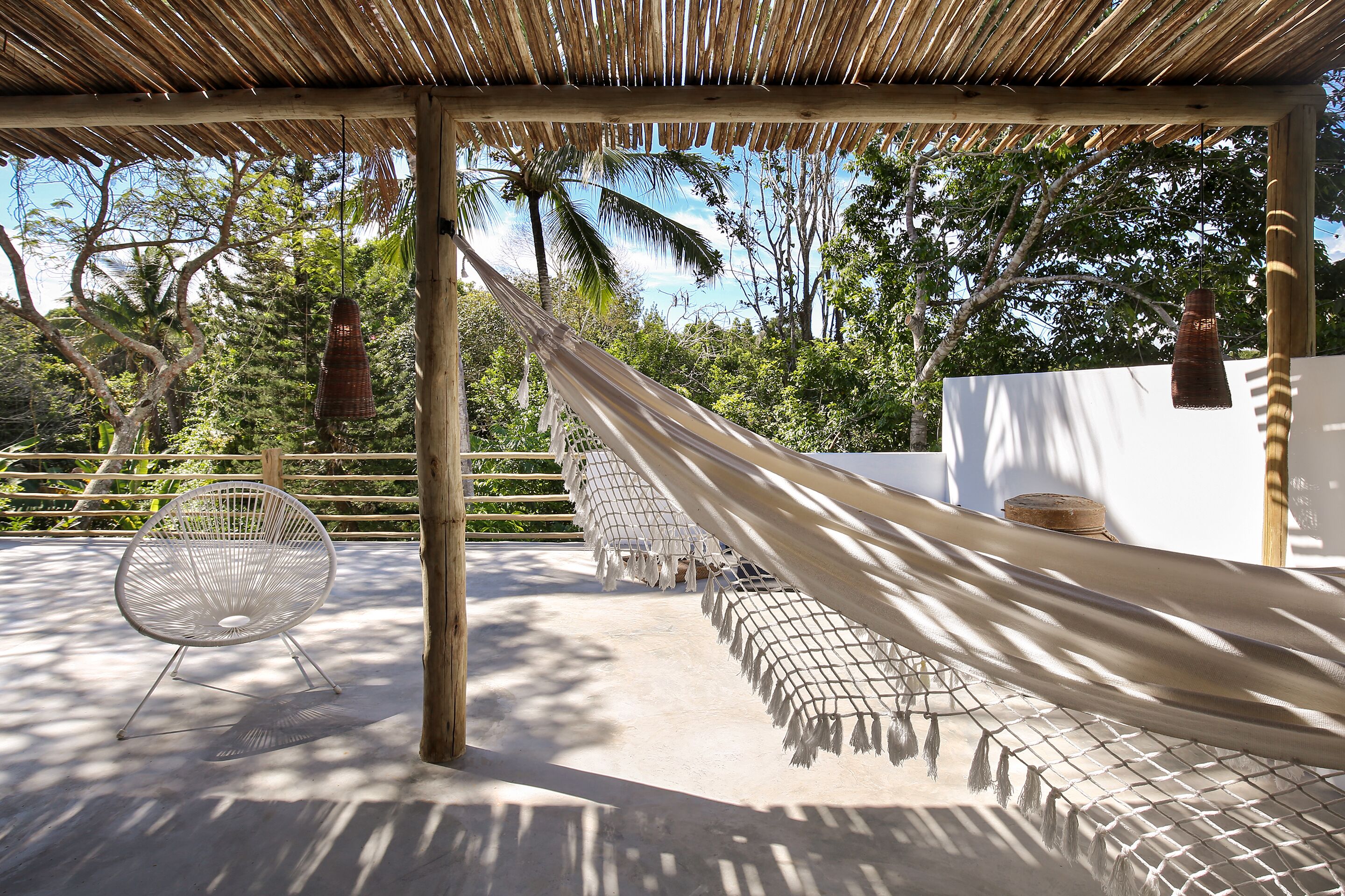 A hammock under a wooden pergola, a white chair, and a white wall with a round object on top.