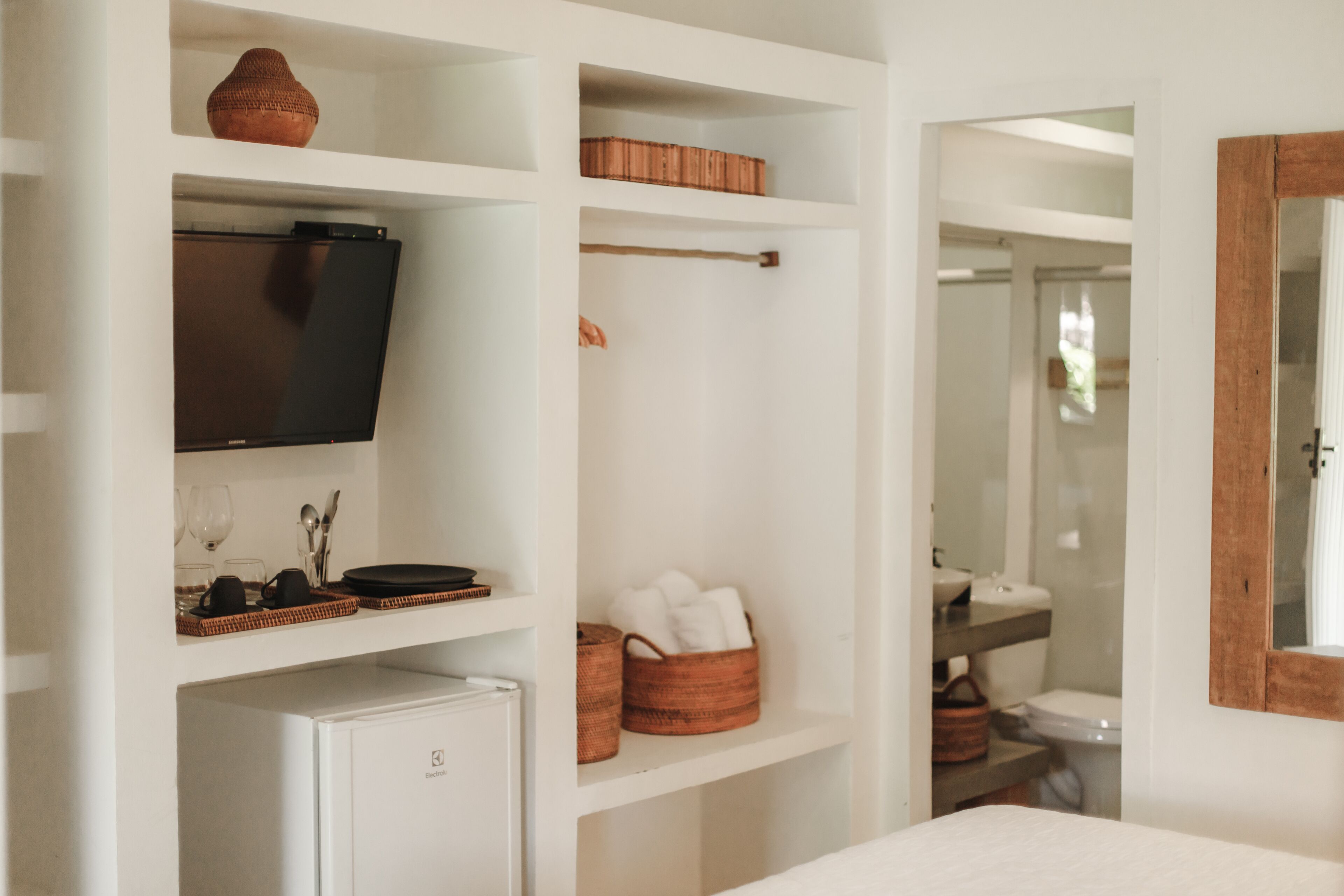A hotel room with a television on a shelf, a small refrigerator, and a bathroom visible through an open door.