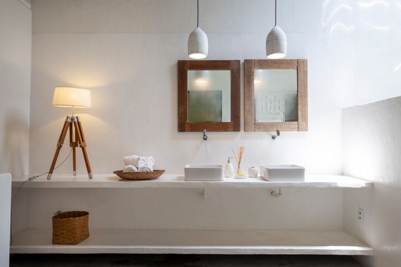 Een badkamer met een wit wastafelmeubel, twee spiegels, een lamp en een mand.