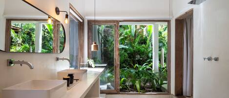 A modern bathroom with a large window, a white sink, and a shower.