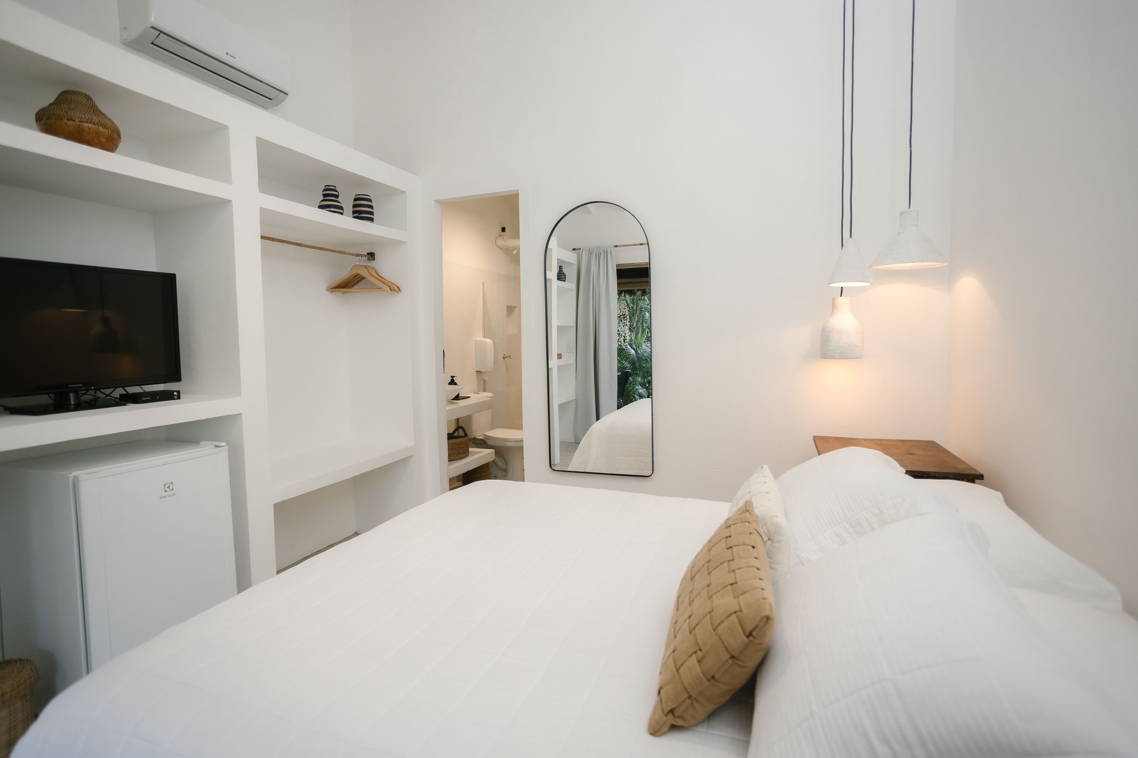 A hotel room with a bed, a TV, a wardrobe, a mirror, and a small table.
