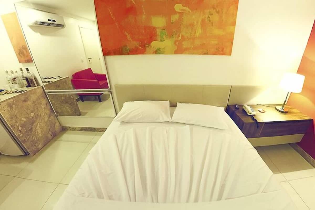 A hotel room with a bed, a desk with a lamp, a mirror, and a painting on the wall.