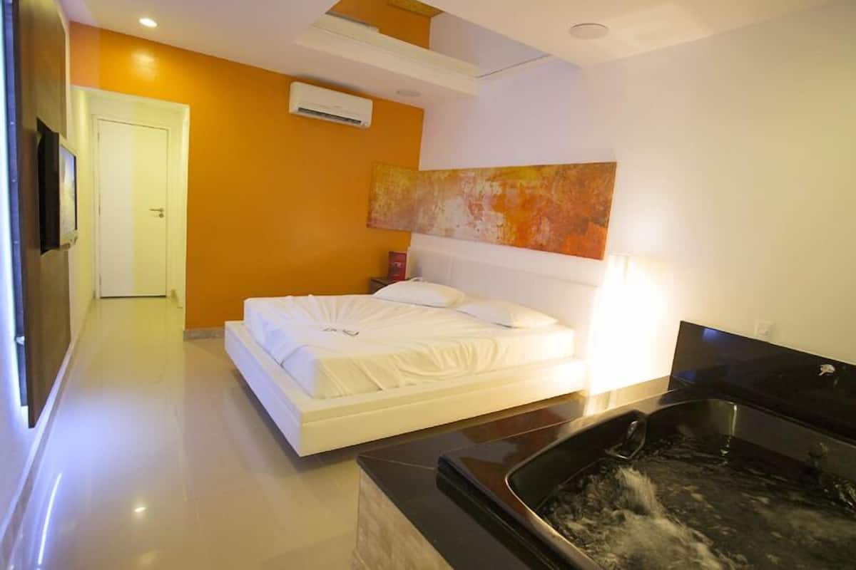 A modern bedroom with a bed, a large painting, a TV, and a hot tub.