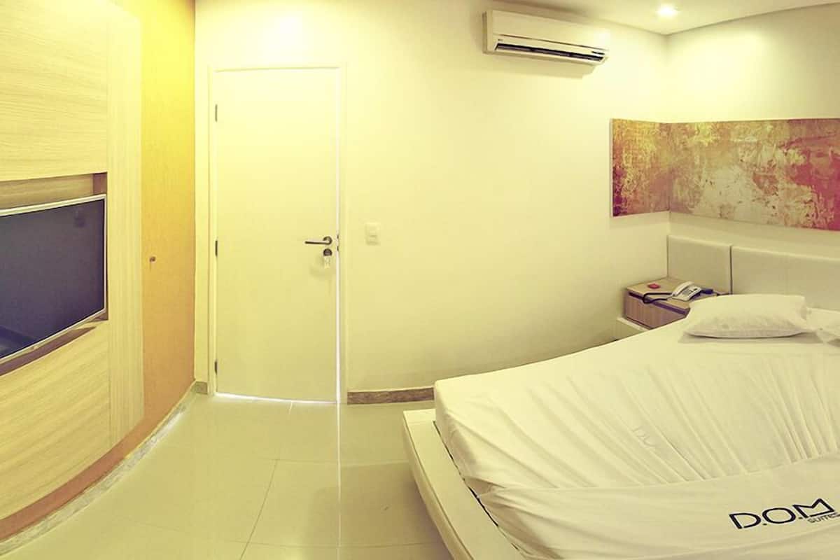 A hotel room with a bed, a TV, a door, and an air conditioning unit.