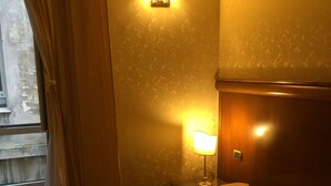 Une chambre d’hôtel avec un lit, une table de chevet, une lampe fixée au mur et une fenêtre avec des rideaux.