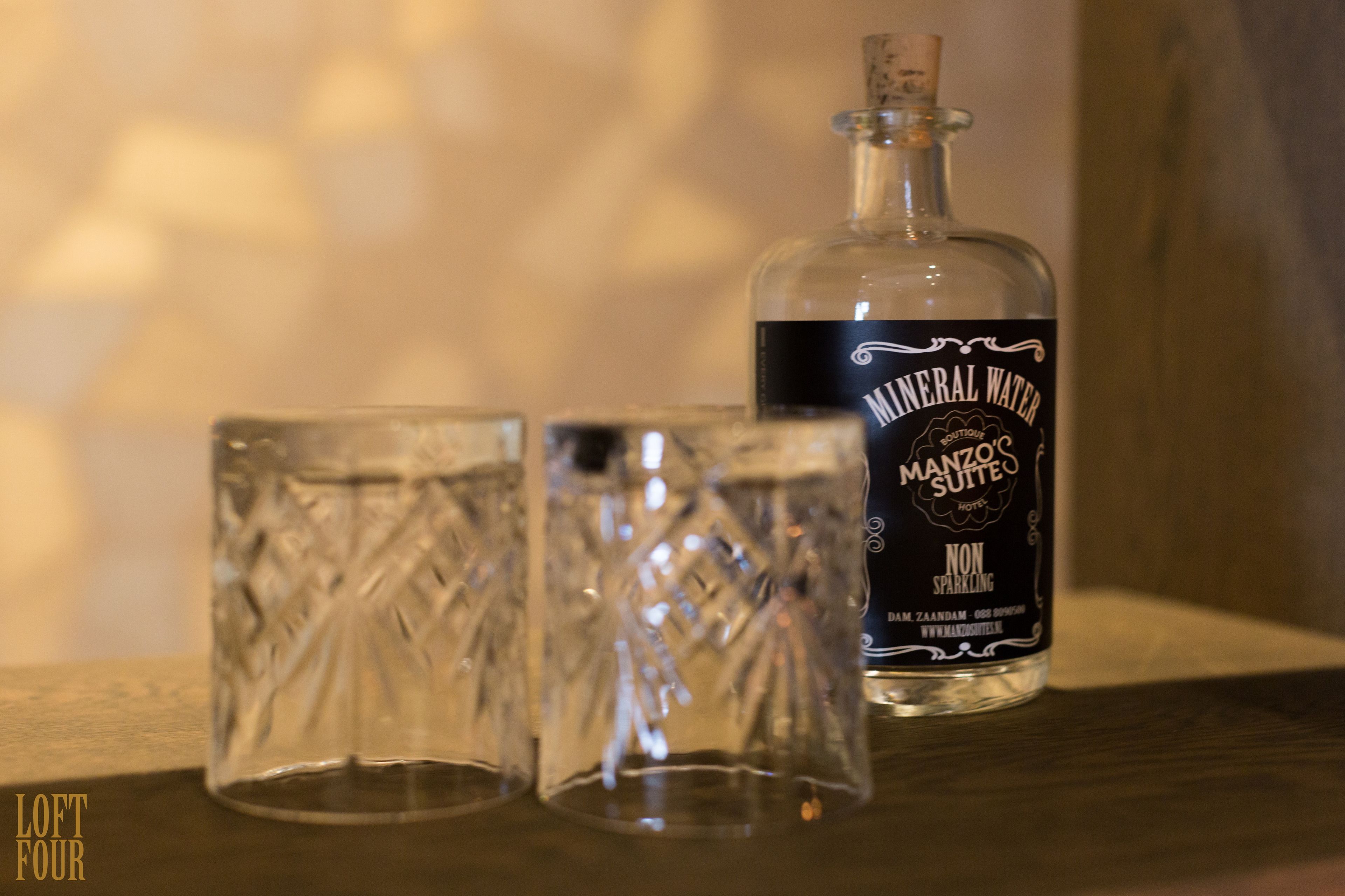 Une bouteille d’eau minérale et deux verres sur une surface en bois.