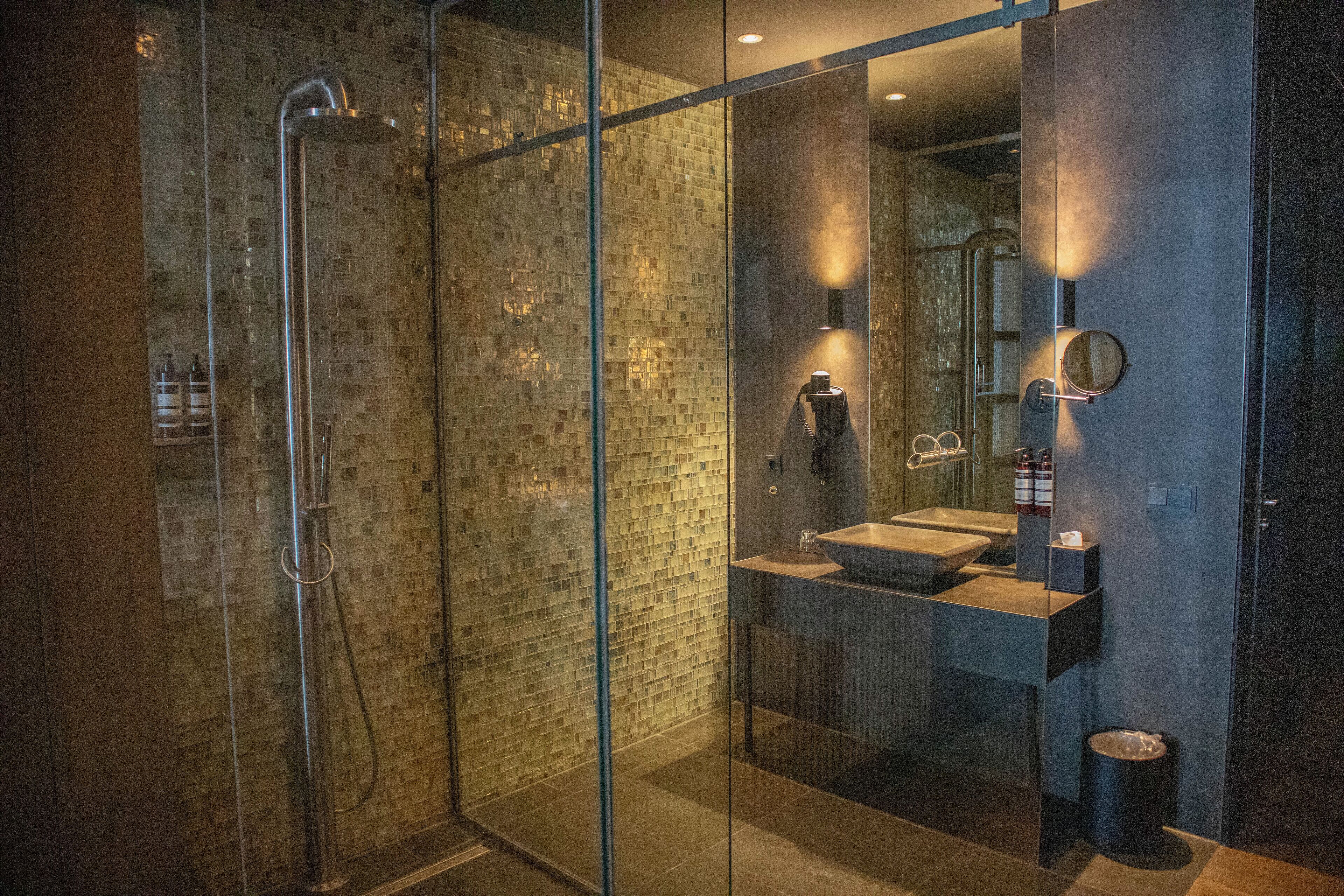 Un baño moderno con ducha de vidrio, lavamanos con pileta y espejo con marco redondo.