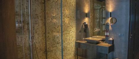 Un baño moderno con ducha de vidrio, lavamanos con pileta y espejo con marco redondo.