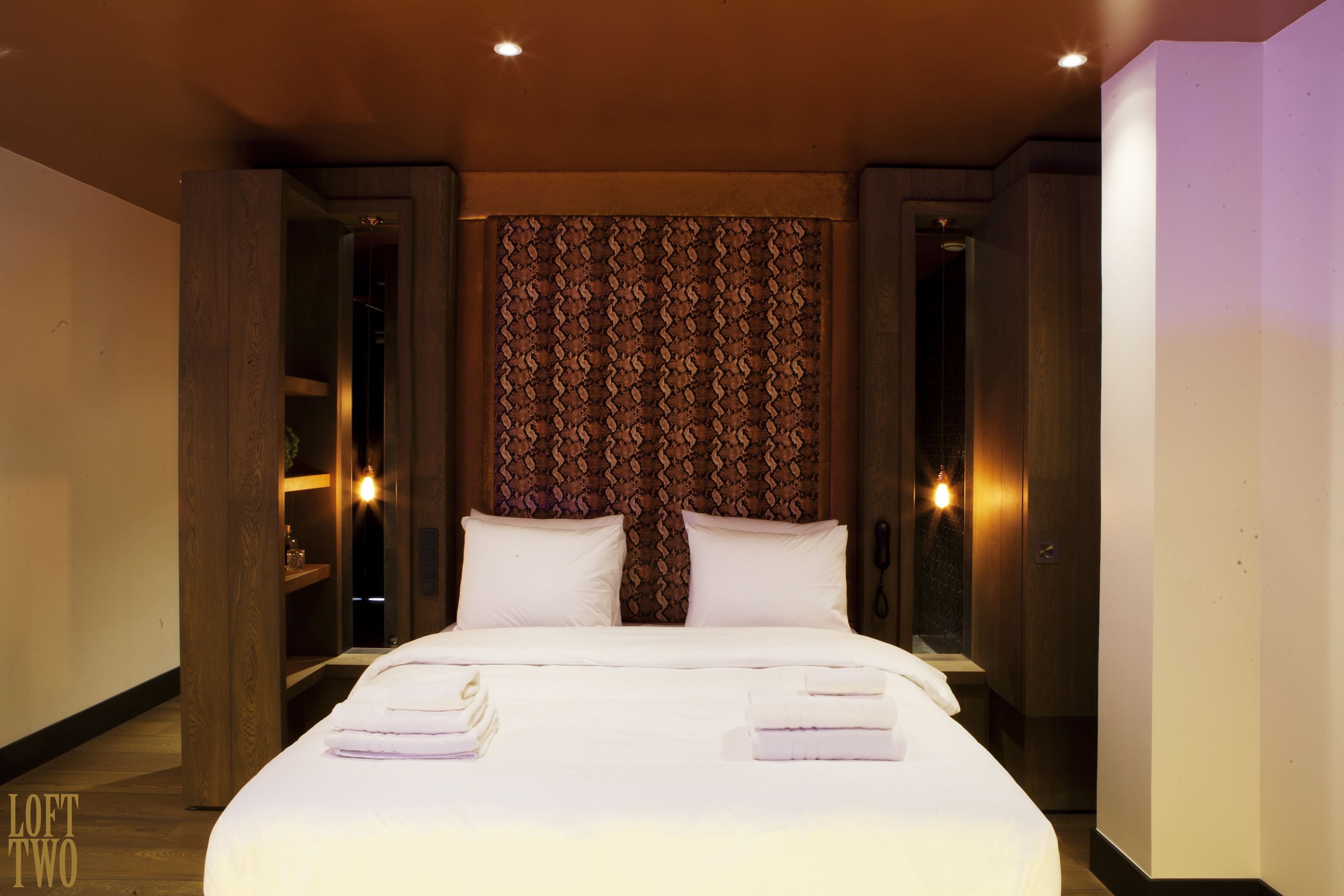 Une chambre d’hôtel avec un grand lit, deux tables de chevet, une tête de lit en bois et un rideau à motifs.