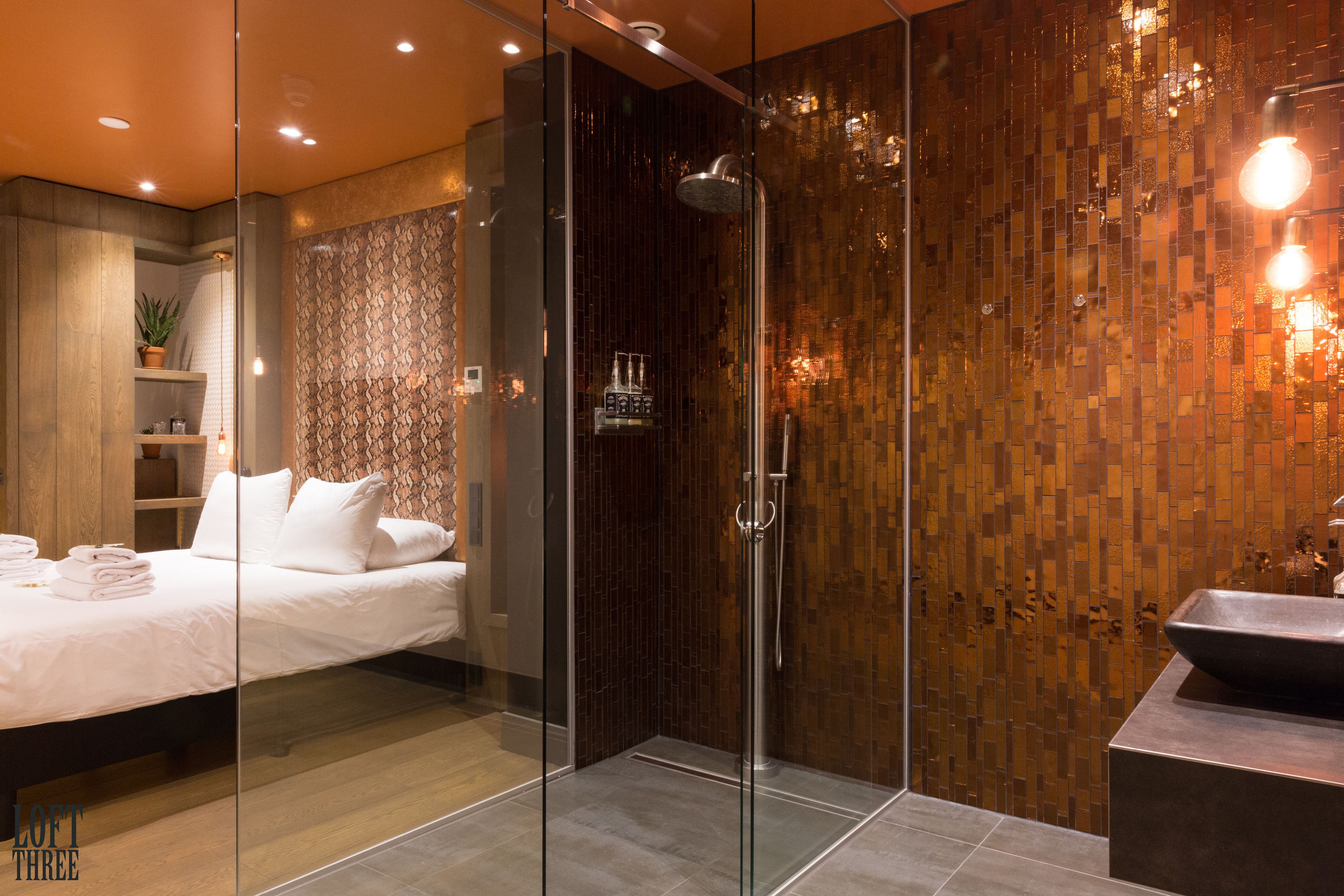 A modern bathroom with a glass shower enclosure, a wooden mosaic wall, and a large sink.