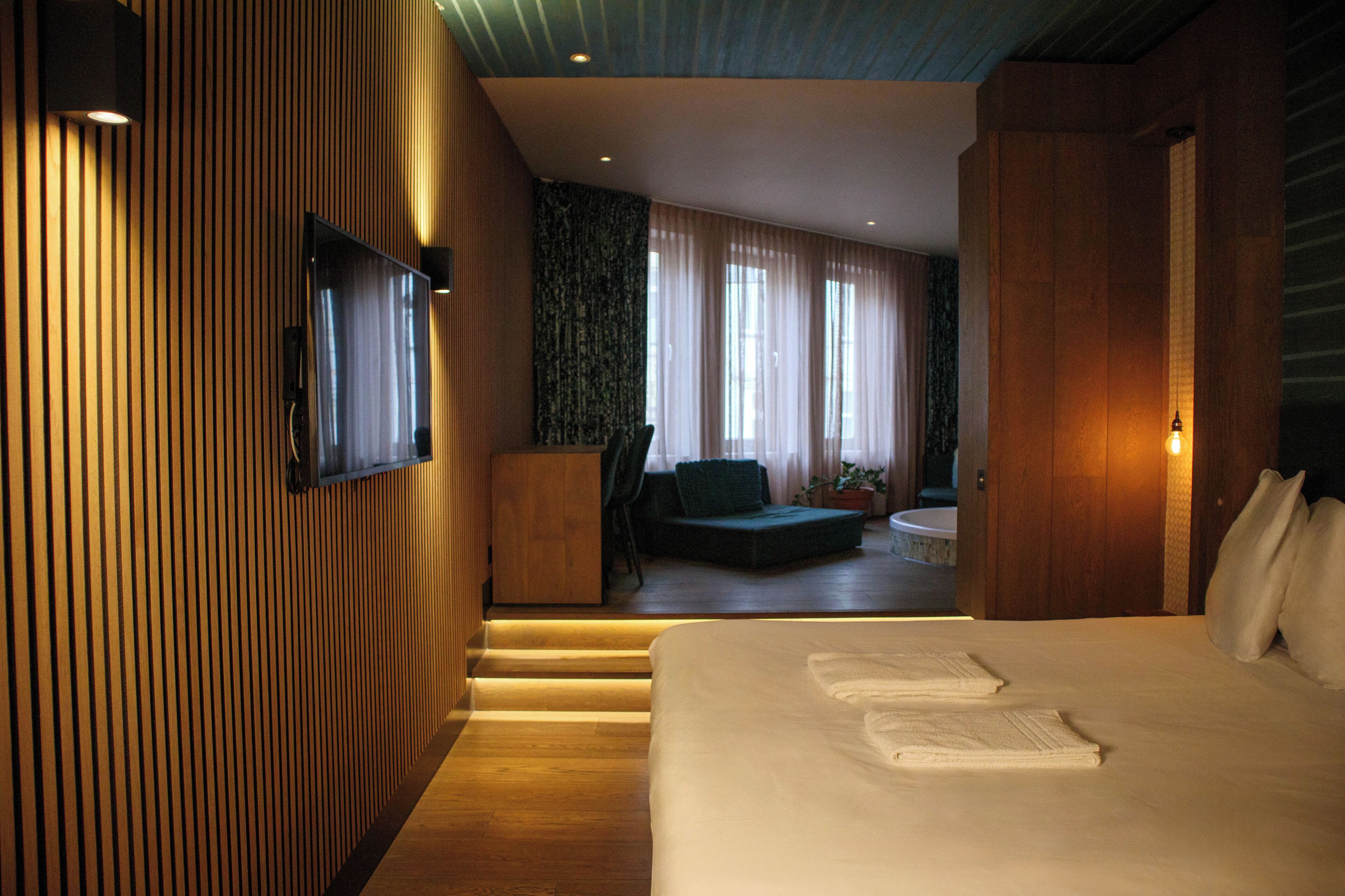 Une chambre d’hôtel moderne dotée d’un grand lit, d’un téléviseur fixé au mur et d’un coin salon avec un fauteuil et une petite table.