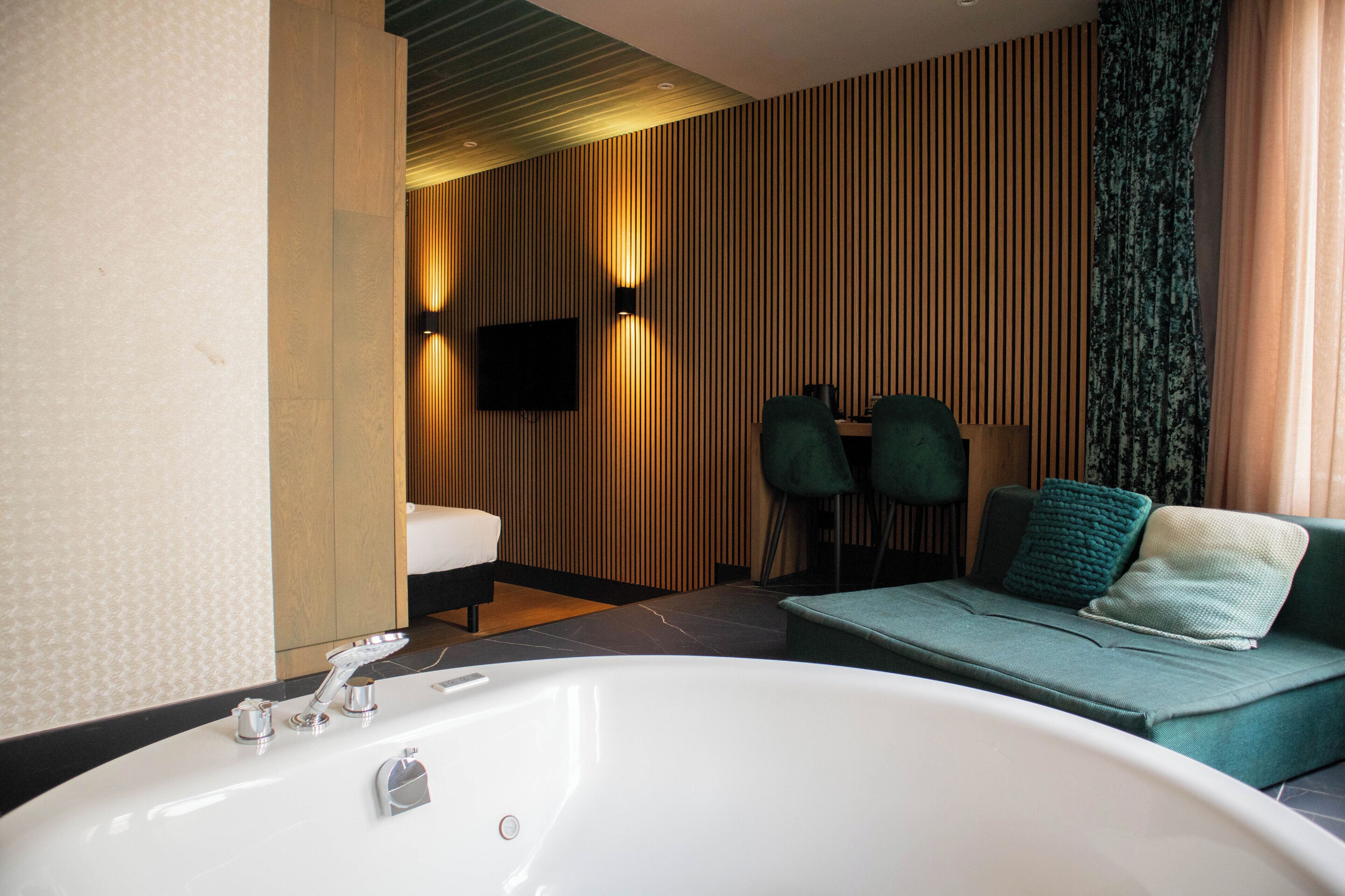 Une salle de bain moderne avec une grande baignoire, un canapé avec des coussins et un téléviseur à écran plat fixé au mur.