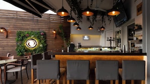 Een restaurantinterieur met een houten bar, hangende吊り下げlichten en een groene wanddecoratie.