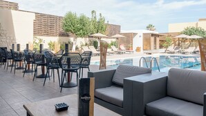Een buitenzwembad met ligbedden, een zithoek met sofa's en een bar aan het zwembad.