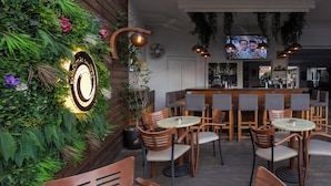 Een barruimte met houten meubels, een televisiescherm en een wand versierd met planten en een bord.