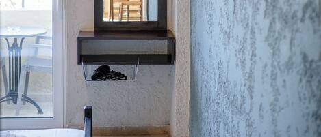 A hotel room with a bed, a bedside table, a mirror, a TV mounted on the wall, and an air conditioning unit above the mirror.