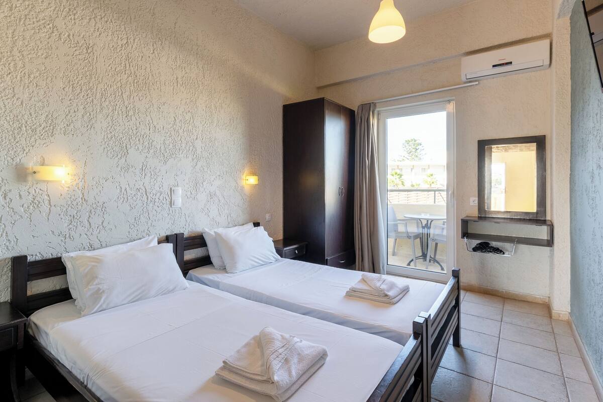 Une chambre d’hôtel avec deux lits, un grand miroir, un petit lavabo et un balcon équipé d’une table et de chaises.