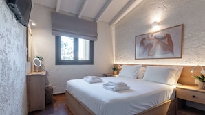 Een net opgemaakt bed met witte lakens en handdoeken, een nachtkastje met een lamp, een aan de muur bevestigde televisie en een raam met uitzicht op groen.
