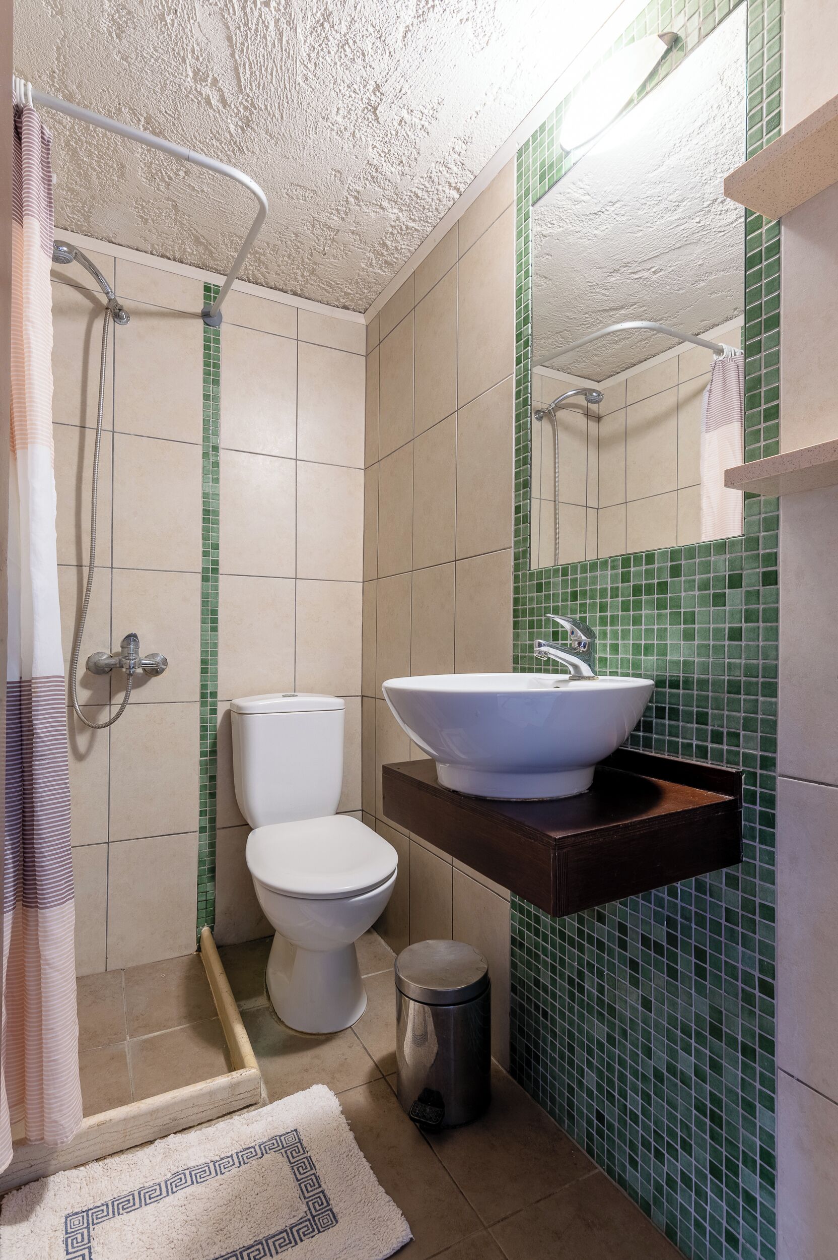 A bathroom with a shower, toilet, sink, and a trash bin.