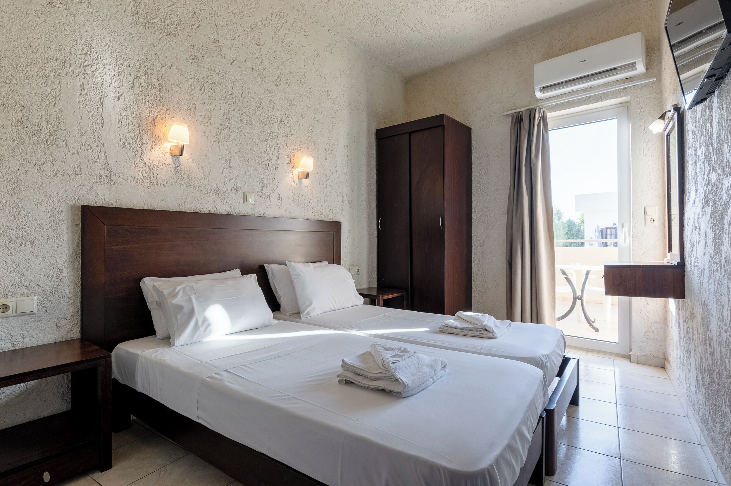 Habitación de hotel con dos camas, un armario, aire acondicionado y un balcón con vistas.