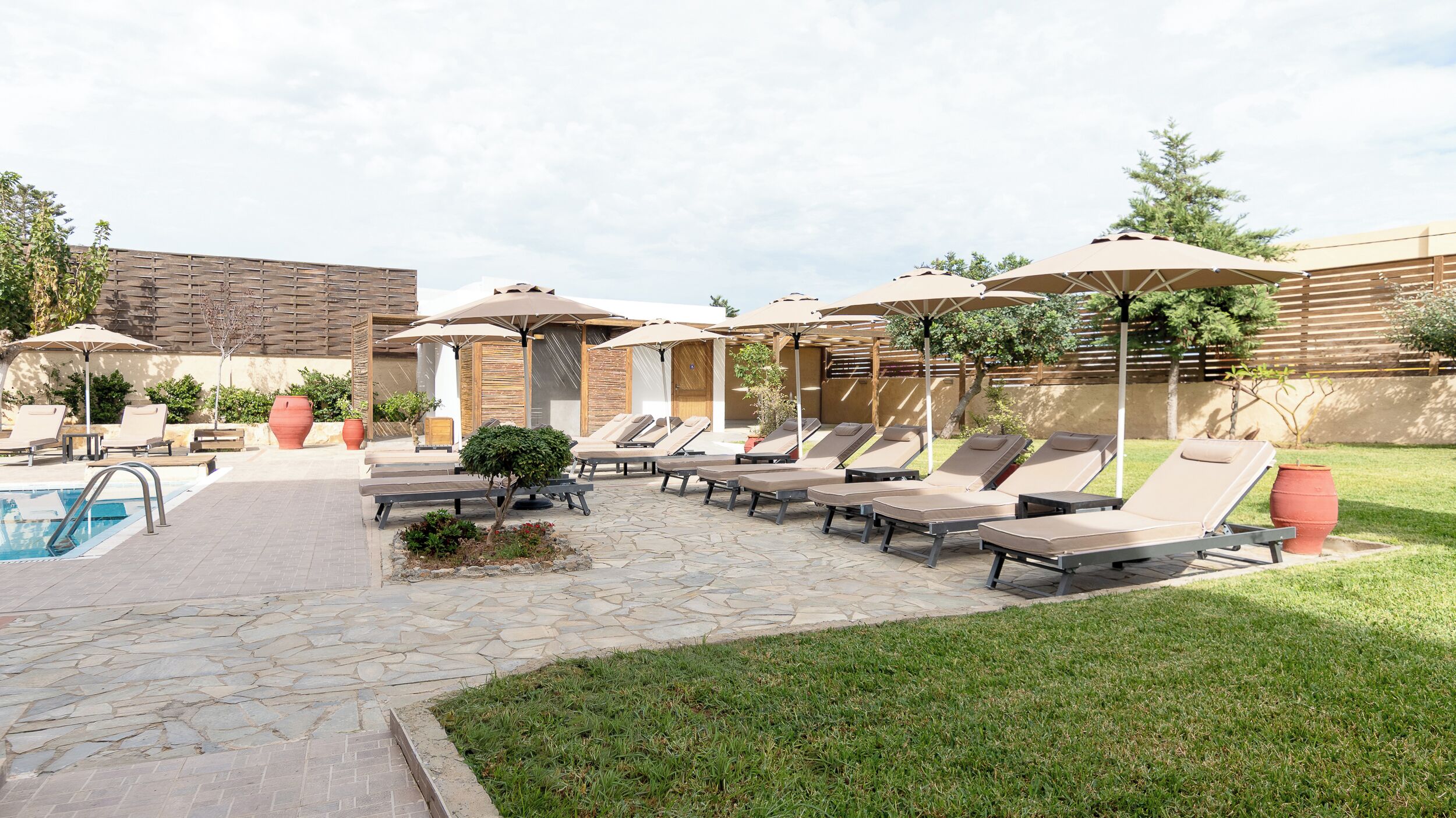 Un espace aménagé au bord de la piscine, avec des chaises longues et des parasols, un chemin en pierre et un petit jardin.