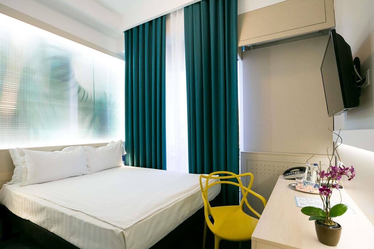 Ein Hotelzimmer mit einem Bett, einem Schreibtisch mit Stuhl, einem Fernseher und einer Zimmerpflanze.