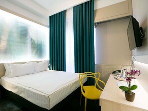 A hotel room with a bed, a desk with a chair, a TV, and a potted plant.