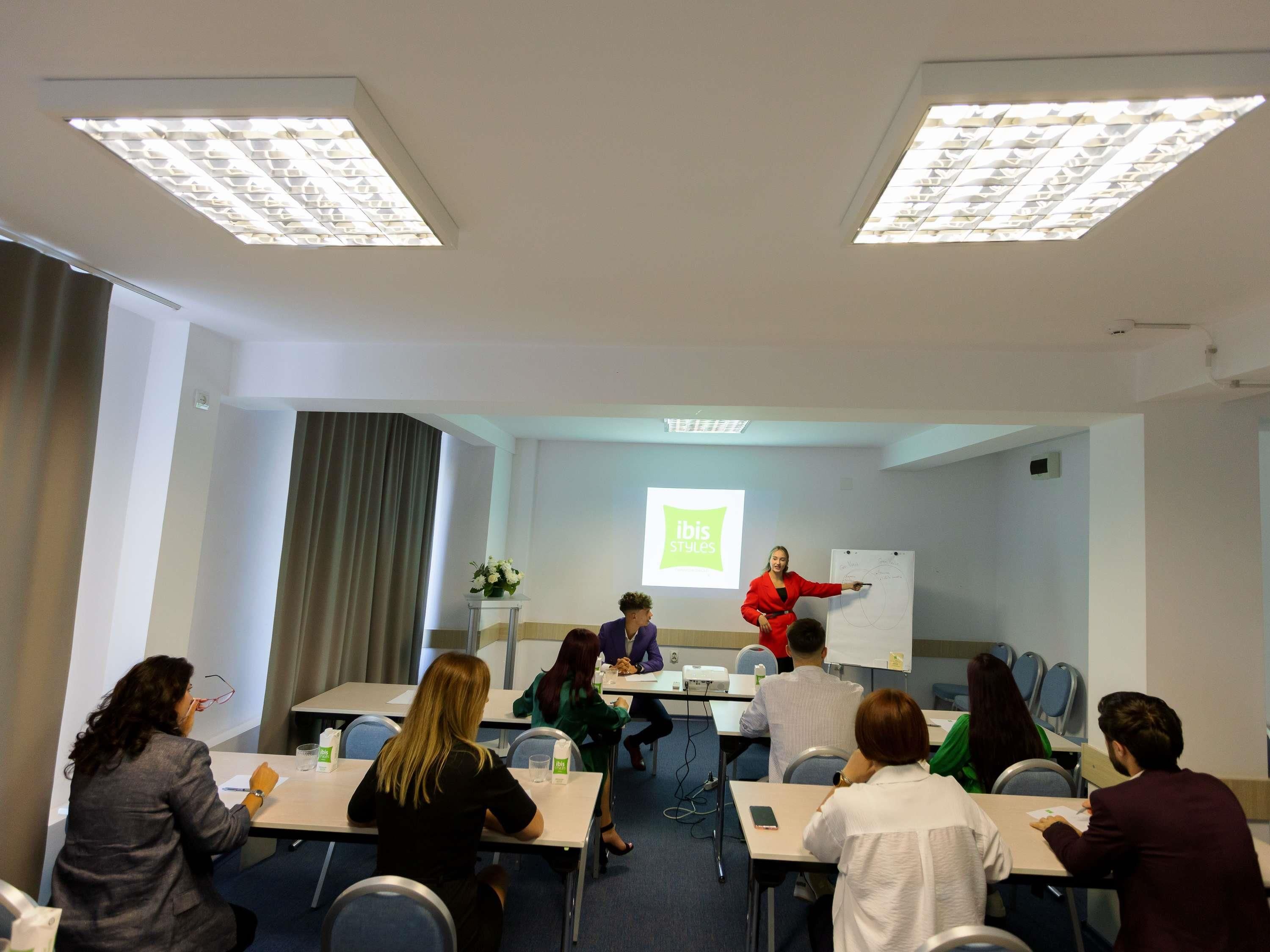 A conference room with a presentation, a whiteboard, and attendees seated at tables.