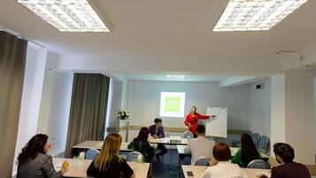 A conference room with a presentation, a whiteboard, and attendees seated at tables.
