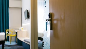 A hotel room with a wooden door, a desk with a chair, a bed, and a television mounted on the wall. - ibis Styles Dunarea Galati (Galati)