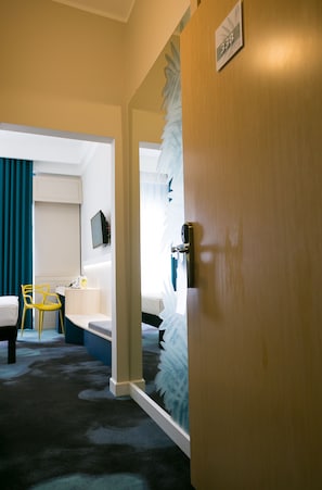 A hotel room with a wooden door, a desk with a chair, a bed, and a television mounted on the wall. - ibis Styles Dunarea Galati (Galati)