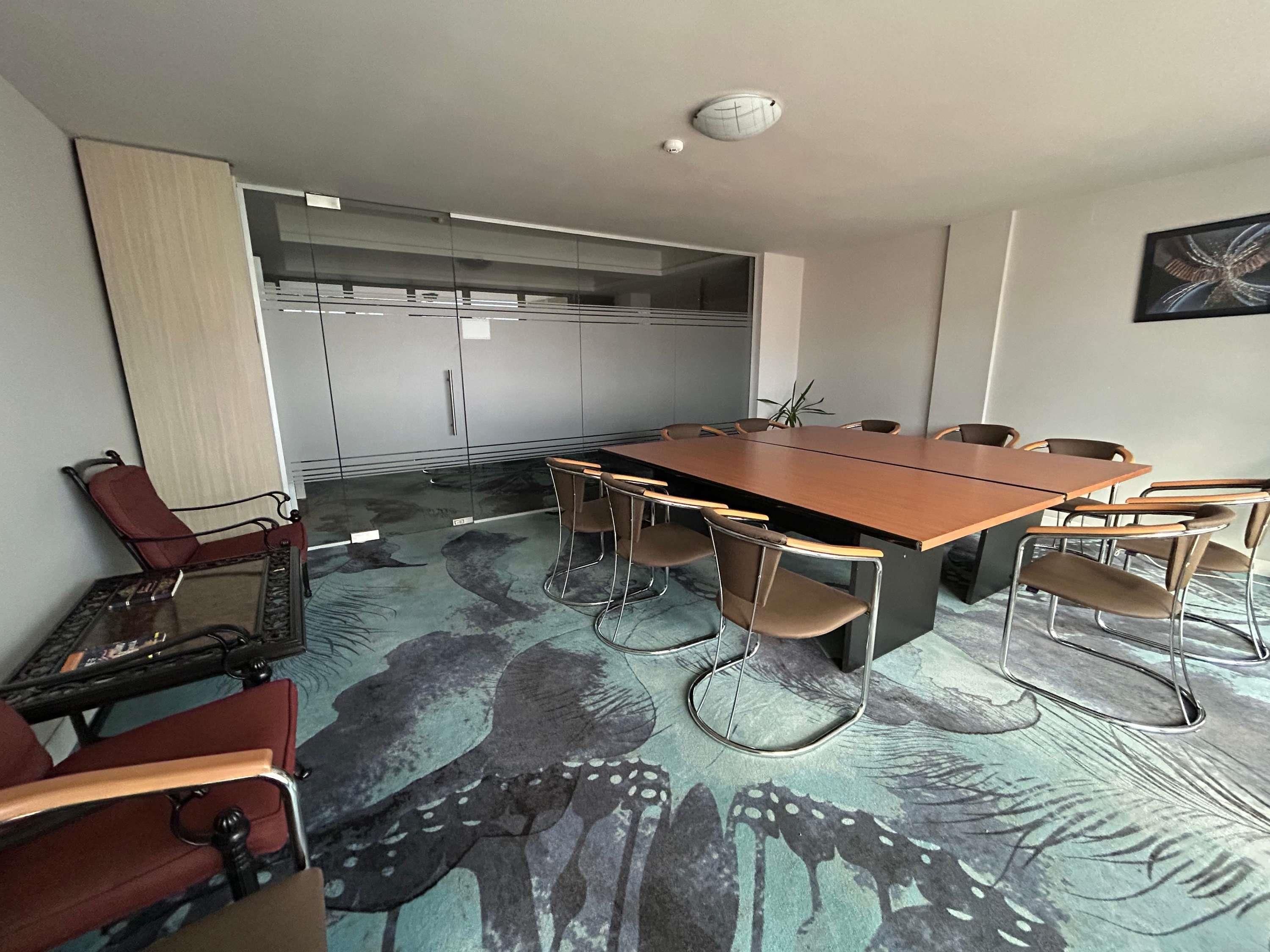 A conference room with a long table, chairs, a red chair, a glass table, and a patterned carpet.