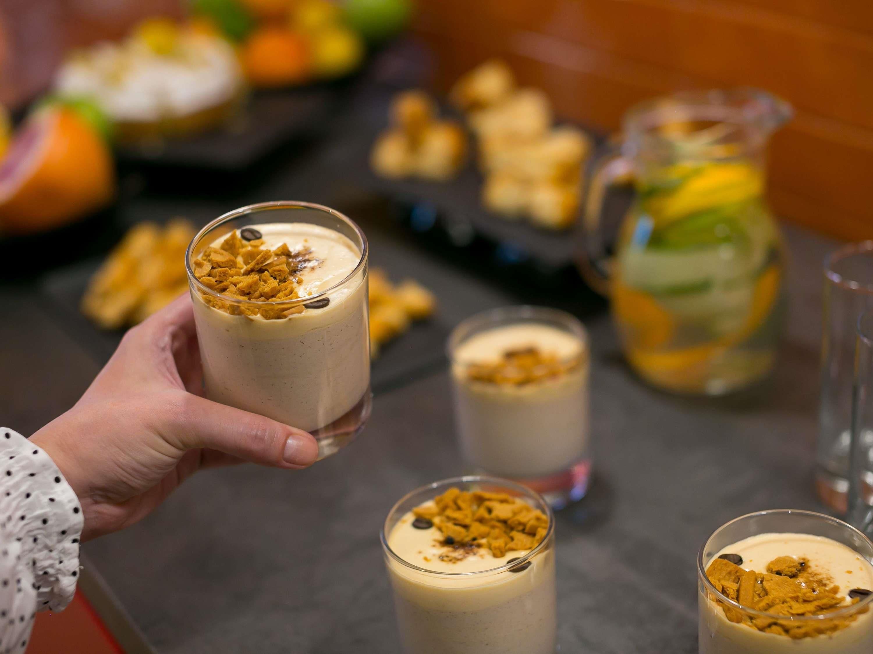 A hand holding a glass of dessert topped with cereal flakes.