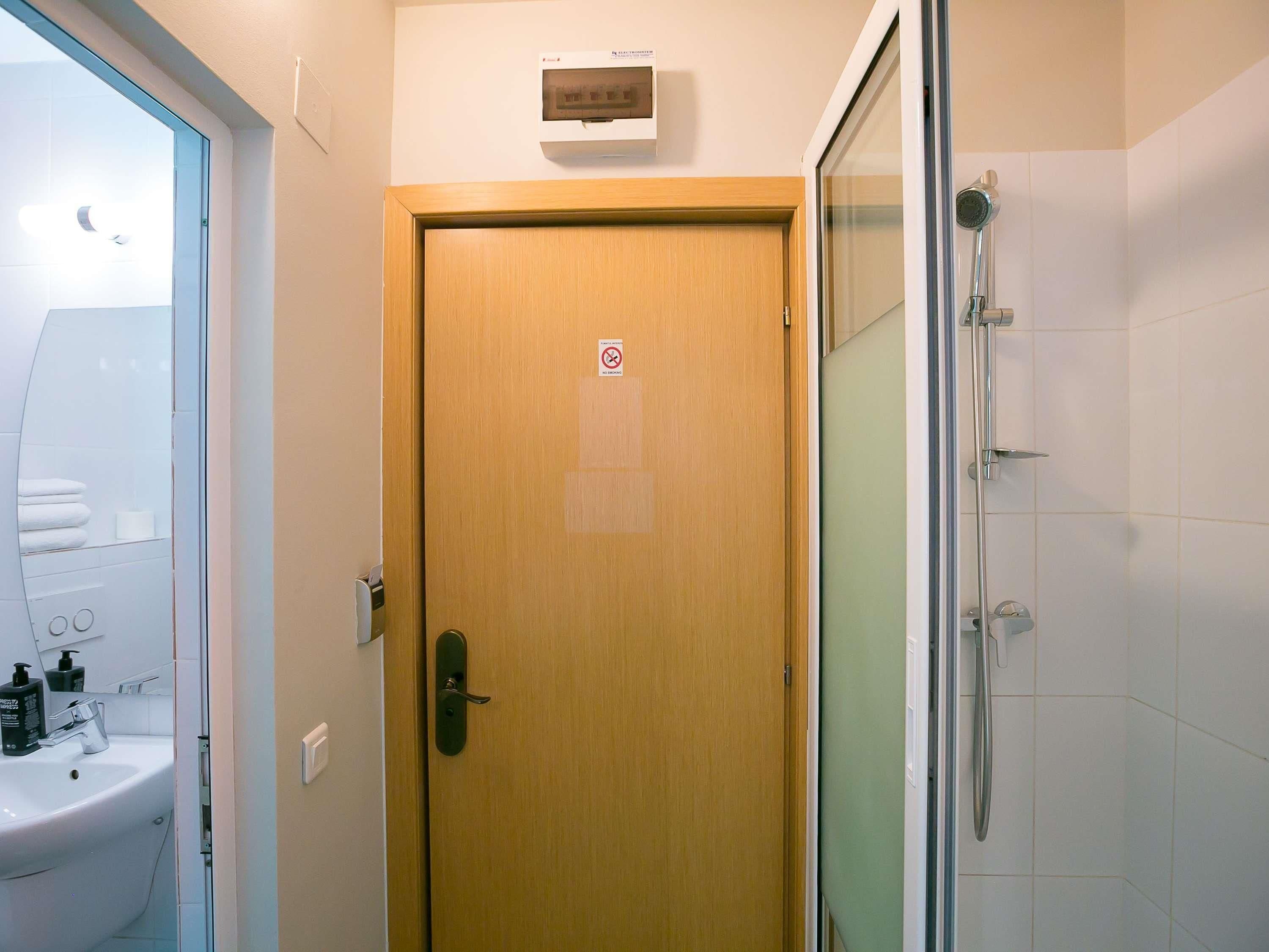 Un baño con puerta de madera, cabina de ducha con vidrio y lavamanos blanco con artículos de aseo.