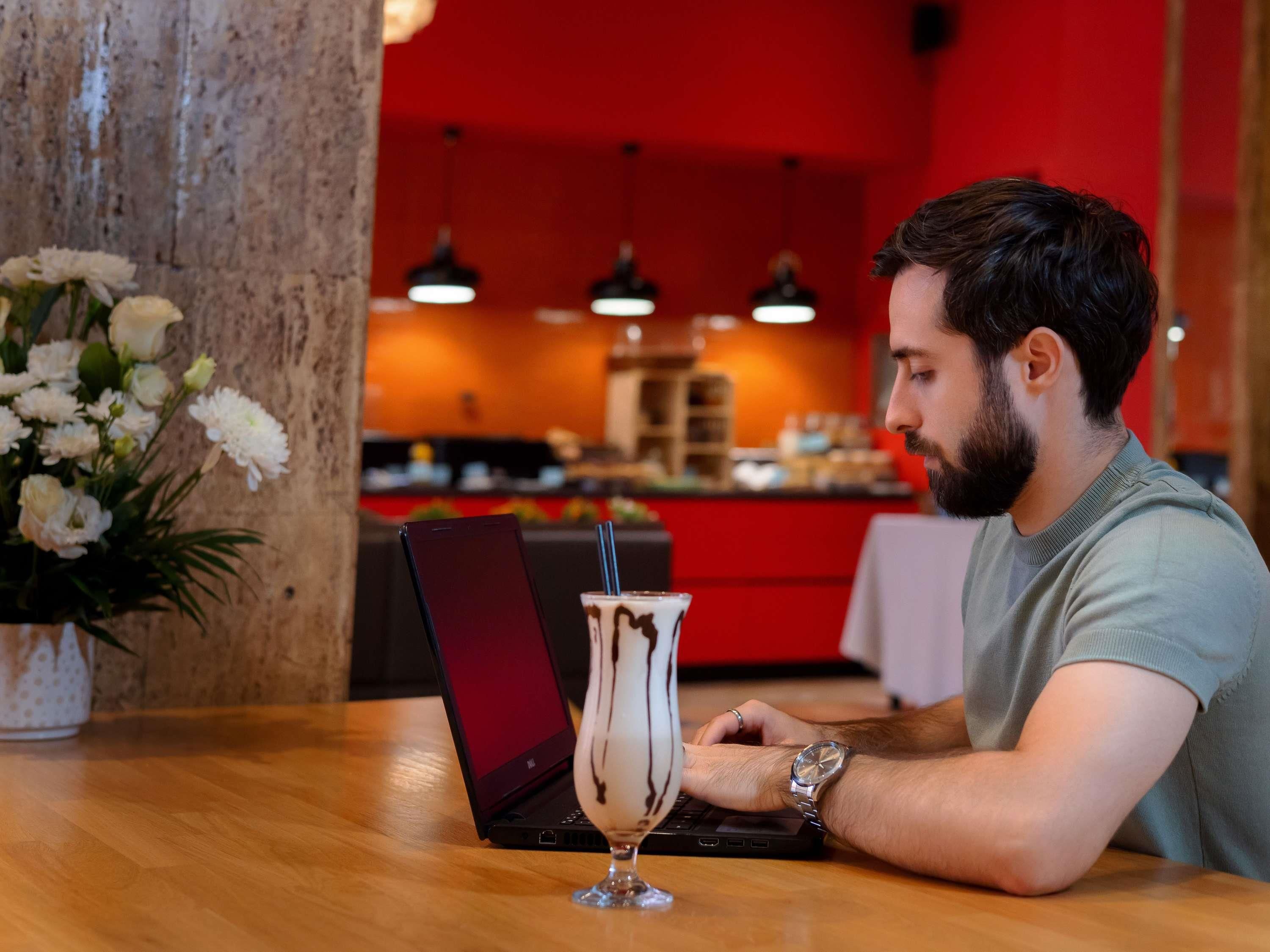 Une personne utilise un ordinateur portable sur une table en bois, avec une boisson dans un verre.