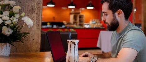 Une personne utilise un ordinateur portable sur une table en bois, avec une boisson dans un verre.