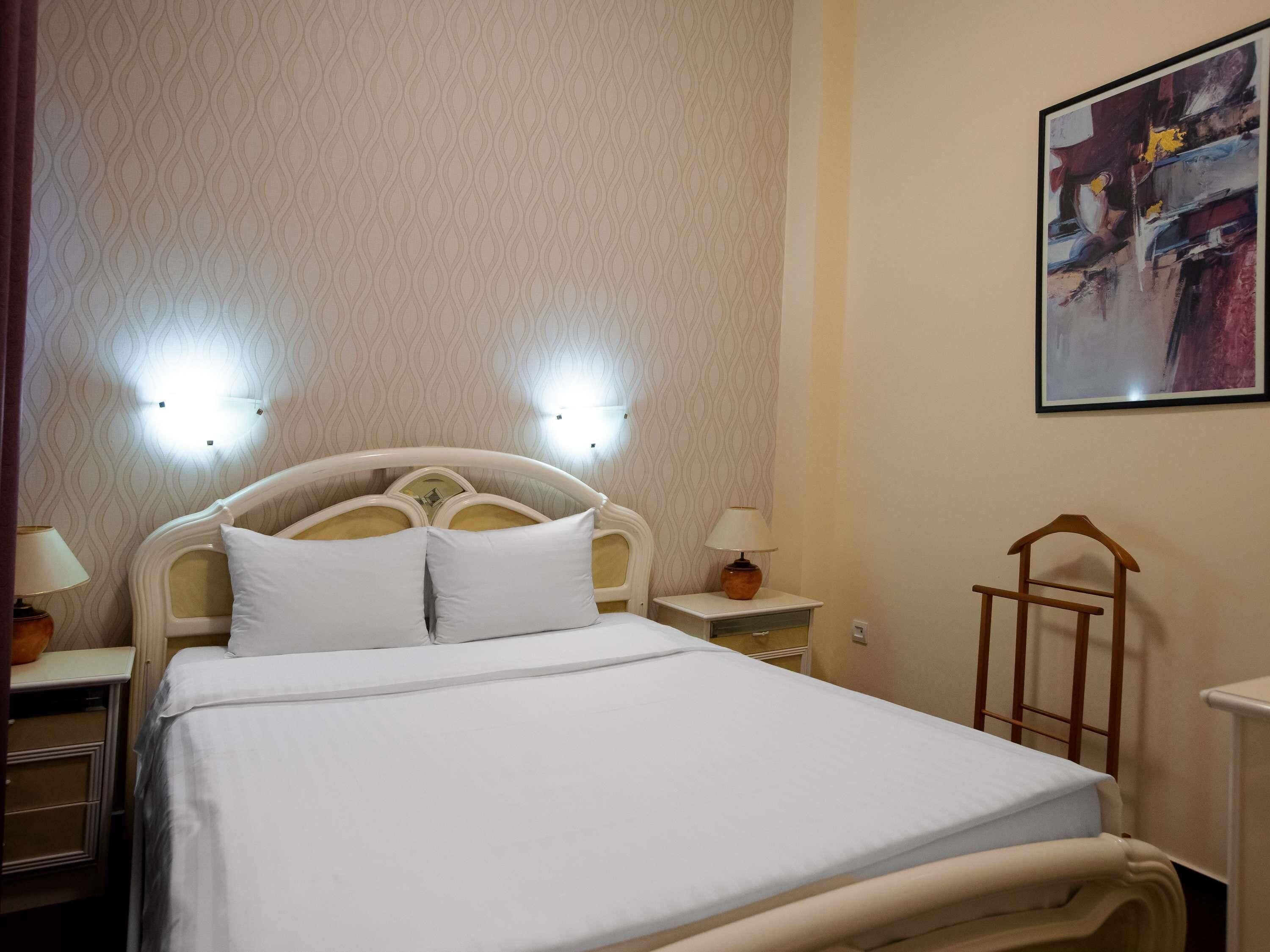 Een hotelkamer met een bed, nachtlampjes, een nachtkastje en een aan de muur hangend schilderij.