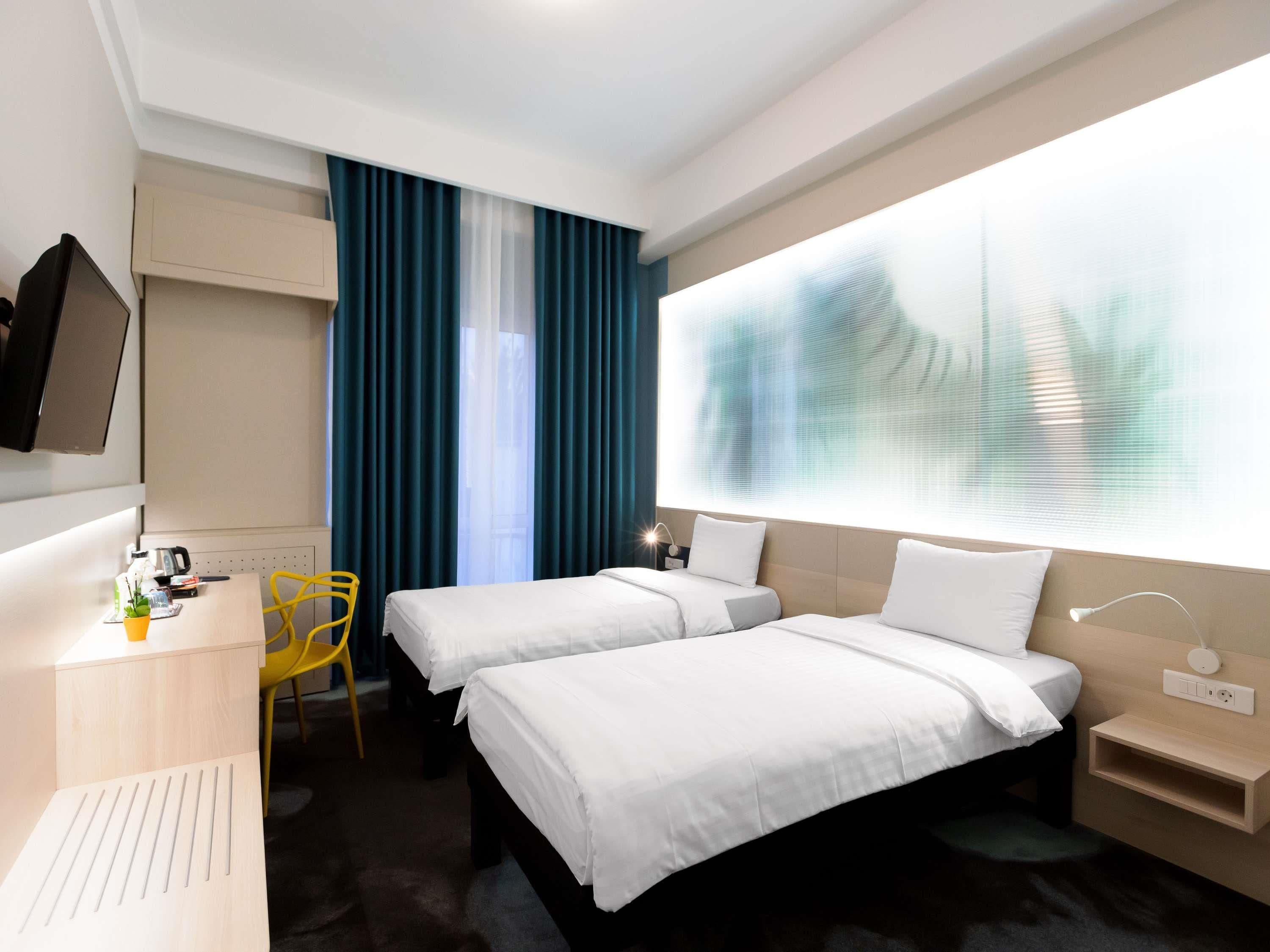 Ein Hotelzimmer mit zwei Betten, einem Schreibtisch, einem Sessel, einem Fernseher und einem großen Fenster mit Vorhängen.