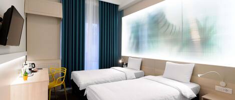Ein Hotelzimmer mit zwei Betten, einem Schreibtisch, einem Sessel, einem Fernseher und einem großen Fenster mit Vorhängen.