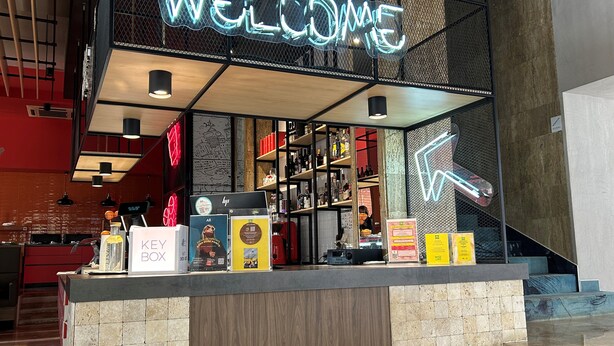 A reception area with a neon 'WELCOME' sign, a KEYSER BOX display, and a variety of products on shelves. - ibis Styles Dunarea Galati (Galati)