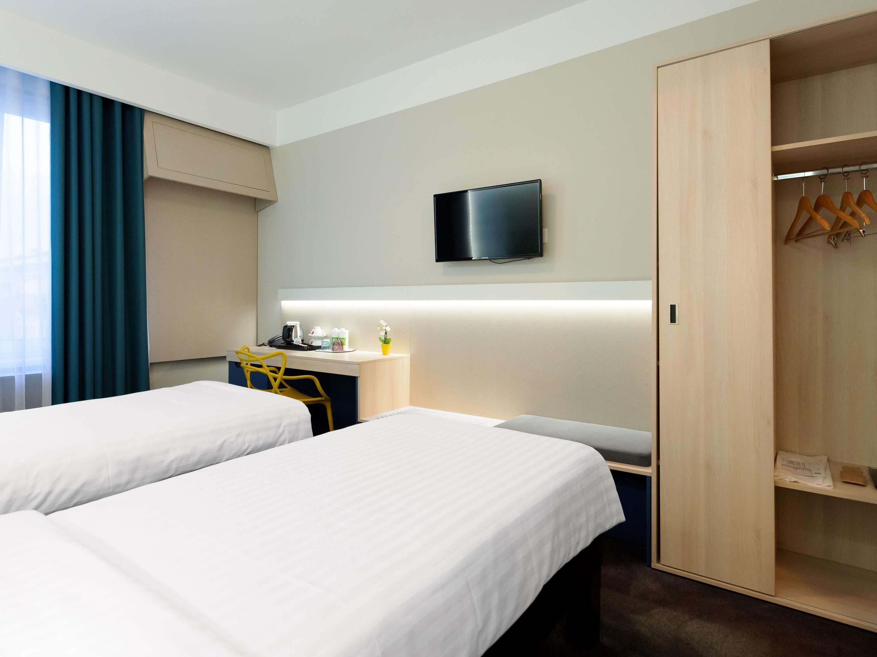 A hotel room with two beds, a desk, a television, and a wardrobe.