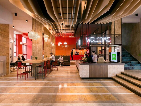 A modern lobby with a reception desk, seating areas, and a staircase.