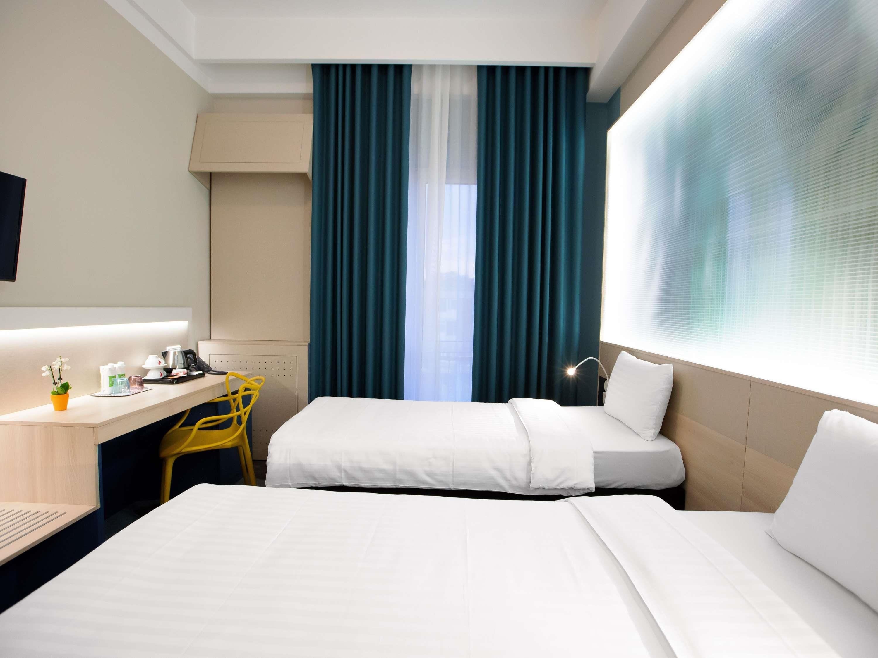 Una habitación de hotel con dos camas, un escritorio, una silla y un ventanal con cortinas.