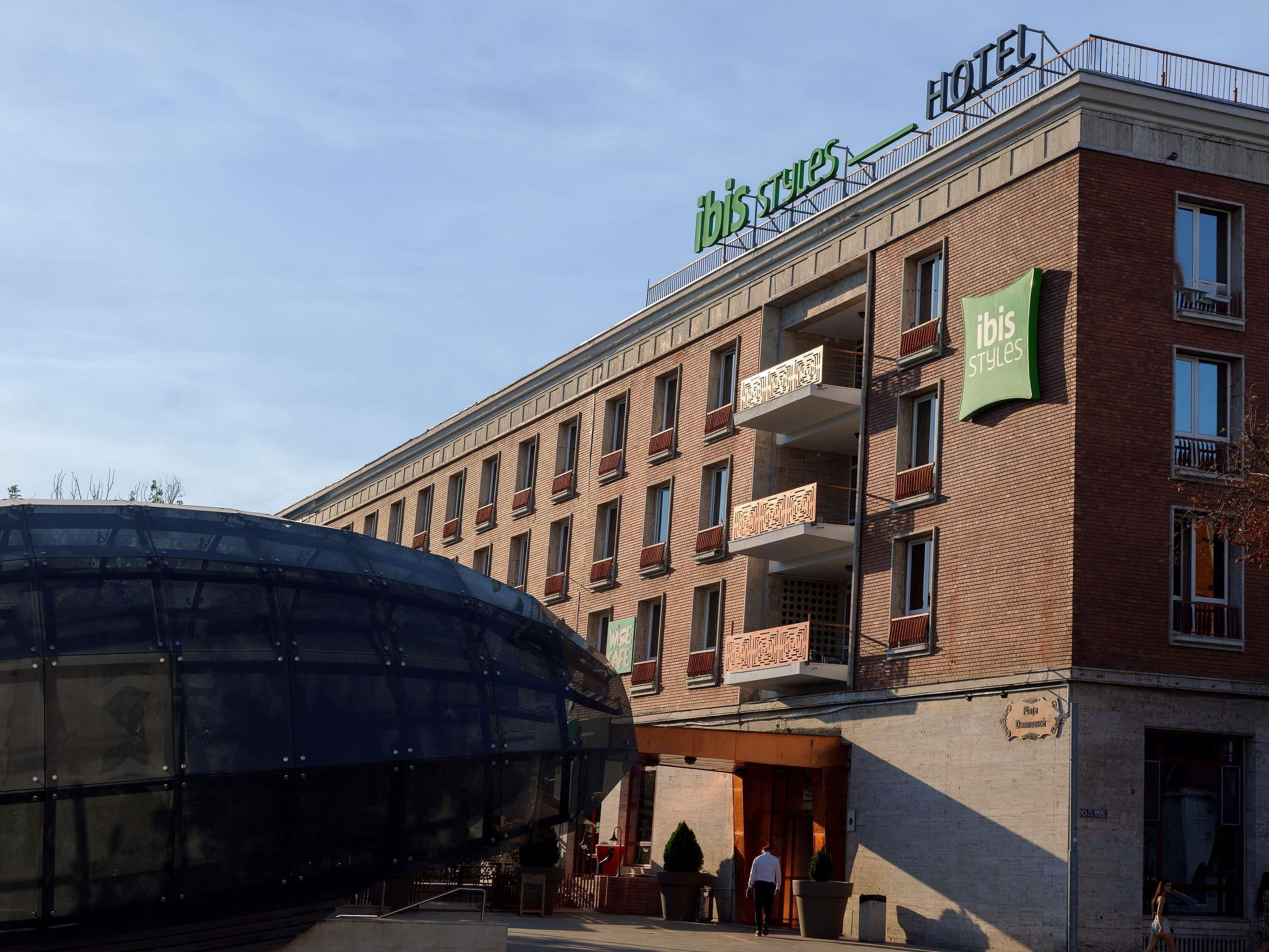 A hotel with a prominent green sign, multiple balconies, and a large glass structure in front.