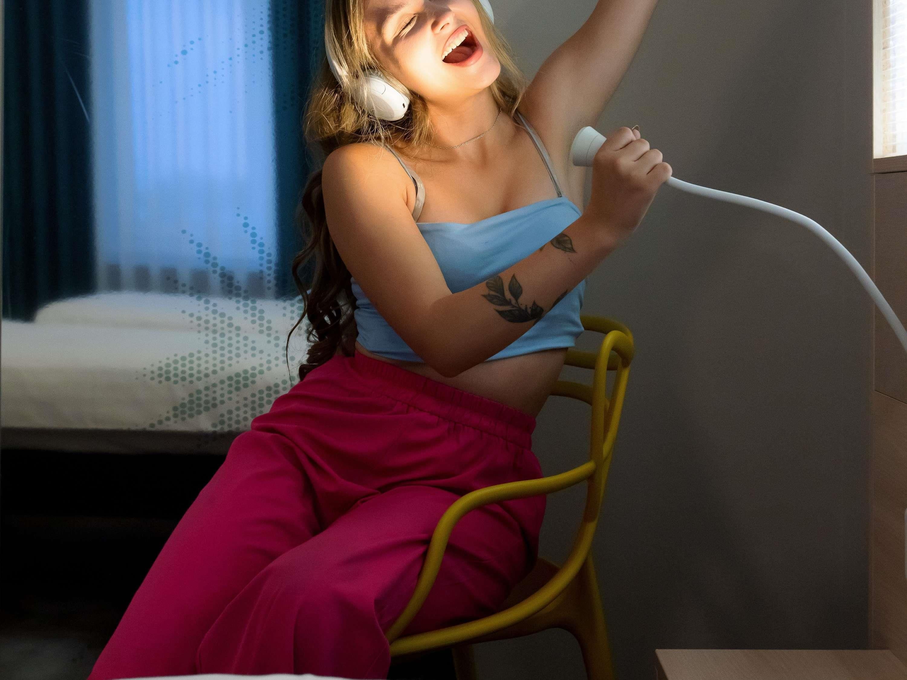 A person sitting on a yellow chair in a room with a bed in the background.
